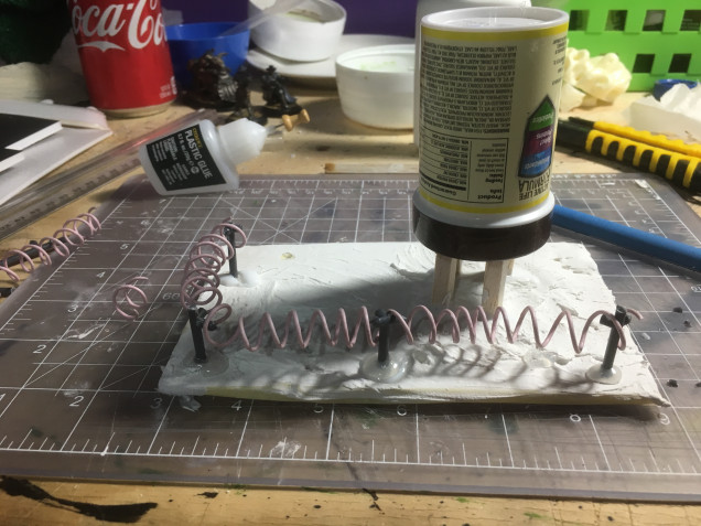 A foam tray with an old charging cord wire turned into barb wire with some sprue pieces for post.  