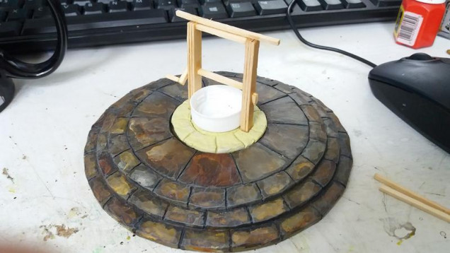 So initial build, I made a circle of milliput the right diameter and textured it and created the flag stones, then while still wet I placed the well wall form (an old bottle cap) and the coffee stirrer uprights.