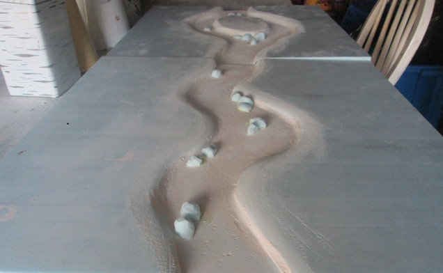 Two river boards, one with an island. After carving out the channel I lined it with wall filler, both to protect the foam in case the Woodland Scenics stuff ate it, and also to texture the bottom (I didn't like the texture and ended up sanding it smooth). I also used polystyrene to make some larger rocks for the banks and river bed. The foam has warped on the island board, but I'll weigh it all down on a flat level surface when I do the first pour of Realistic Water. 