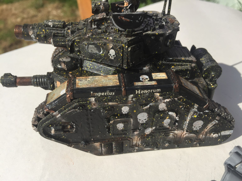 The Commissar’s Leman Russ Conquerer WIP. This was spray painted chaos black and then I experimented with flicking yellow paint using an old toothbrush to give a unique pattern which differentiates this black tank from Glofski’s Black Deff. I scrounged as many white skull transfers I could find and applied all over the tank. I created mini doctrine messages to adorn the tank track covers by scaling down images of parchments written in Latin and printed these out using a computer. I’ve reblackened a space at the front on each side for a further bit of freehand. The commissar is from Forge World OOP but nice to get a bit of close up detail on him. I need to make the banner, mount a trooper companion and finish off transfers and fine details before mounting on its base and weathering.