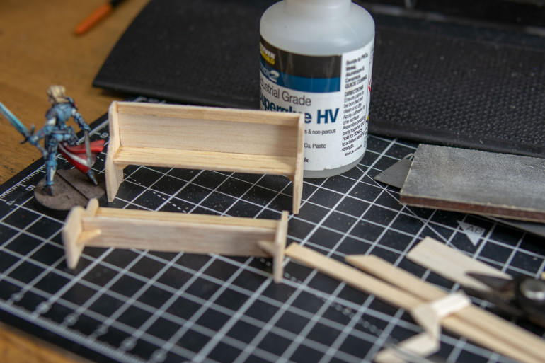 I also wanted to break up the walls in the background. I thought about reliquary’s or something high tech but decided to keep it old looking e.g., modern for today or back to medieval.  I googled “medieval church pew”. It seems like these used to be very simple. I remember these as a kid, torture chairs. They are not designed for sitting. Evil as a kid they were too narrow. The ones in my church had a gap where the kid behind they could pinch your arse or put stuff down your trousers. Also, apparently that doesn’t matter, and you should not break other kids nose in a house of god… I didn’t need the hymn book stand on the back and copied the general design making this out of 1.5 and 1mm balsa wood. I didn’t have or plan for them I just measured to the knee of old Joan that set the hight of the seat and to the armpit for the hight on the bench. I corrected the childhood design flaw. And assembled using superglue.   I just used clippers to make a small angle jog then cut the sides to make them the same and rounded them with sandpaper.