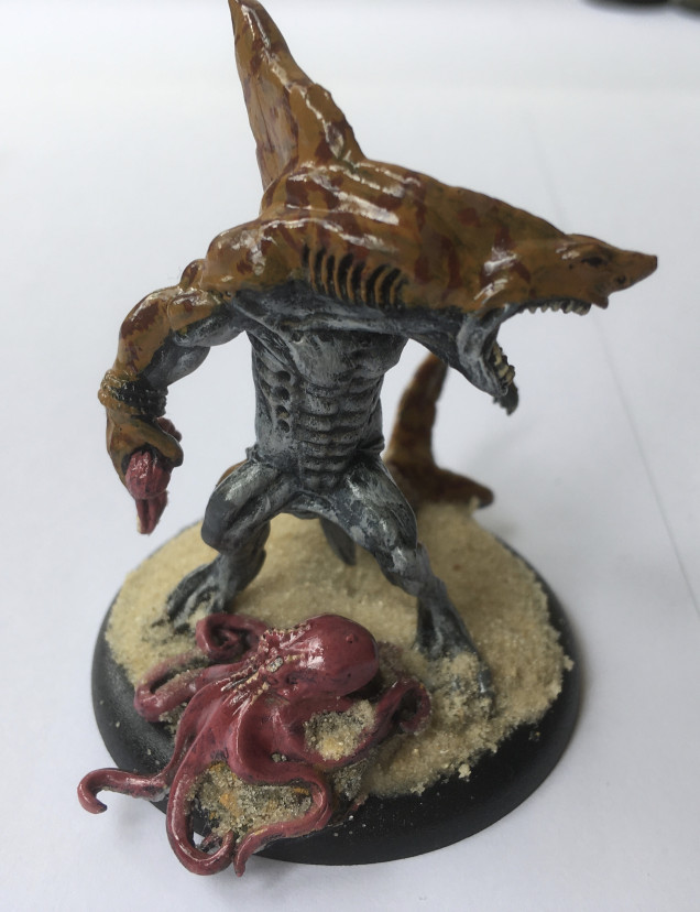 The Danger from the depths… Model chosen Reaper Miniatures Wereshark  SKU: 02890 Sculpted by Jason Wiebe plus Octopus from FAMILIAR PACK VII SKU: 02948 Sculpted by Julie Guthrie. I’ve tried to paint this guy with tiger shark-like pattern for the skin. I’ve also given a good lick of ‘ardcoat to give a glossy, wet finish. Mini is mounted on a 50mm lipped base with bleached kid’s ‘play sand’ mounded up with watered down PVA glue. 