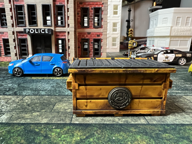 I chose yellow and green for the dumpsters, with metallic parts in GW Leadbelcher and top in flat black, to simulate heavy plastic.  I also had fun with tags/placards. my advice is to use actual street arts/photos as inspiration. A solid GW Agrax wash followed by topical weathering with Agrax and Typhus Corrosion using a small brush finished the job.