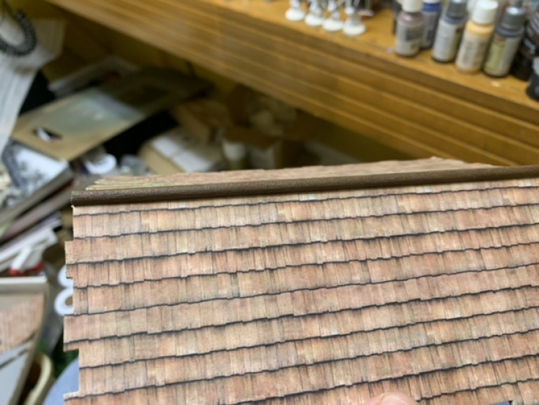 I used a wooden dowel cut to size and then painted it to match the framing. I then glued it to the rooftop to cover up the join lines of the paper and to form the roof peak. 
