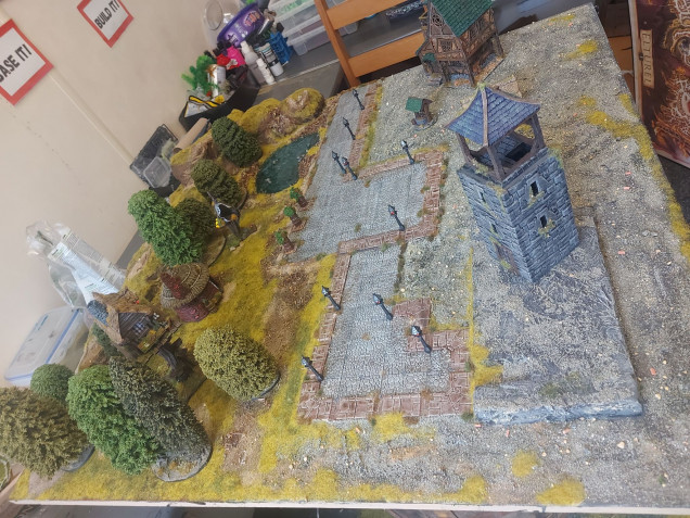 I painted up some Dungeons and Lasers lamp-posts, and they look perfect on this board. I spaced them out around the town square, and then began placing some trees and buildings, to get an idea of how it will look when set up properly. I decided I need another 2 or 3 buildings on the town side, so time to look through the Tarok STLs and find a couple I like. I'm also tempted by the windmill, but this board needs to be ready by the 24th, so I shall have to see how time goes. 