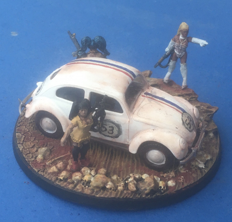 Miniatures chosen: Wargames Foundry: SV015 - Mistress Trudes Girls ‘Fifi’; SV016 - Junos Crew ‘Juno’ (converted into driver); SV038 - Mistress Medusas’ Gang - ‘Mistress Peach’ and ‘Mistress Pandora’. ‘Herbie’ customised from a Tamiya 1/48th Volkswagen Type 82E Staff Car model kit. Diorama mounted on a Legend Games 100mm round skull base. 