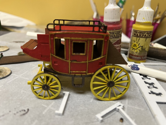 I then covered the pink with Demonic Yellow. It generally took only one or two coats to cover the pink, which is far easier than trying to cover the Rough Iron color. You can also see here the coach has had its top rails, rear luggage and coachman’s area  installed. 