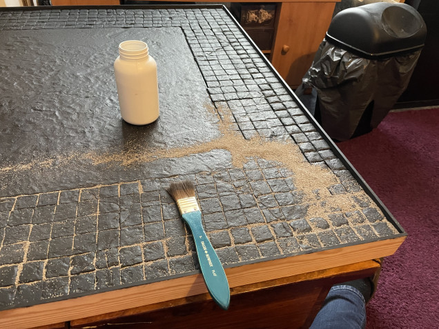 So I brush on some fine sand into the board it fills some of the gaps between the flagstones on the board. After brushing it on I then gave it a spray of 50/50 water and PVA to seal it in. I know there’s better mixtures I could use for fixing it in place but honestly I’ve other things that will be layered over it and will fix it in place. You’ll notice there’s the 2’x2’ flat area in the middle of the board. Two reasons for that I’ve played Bushido before and would like to get back into it again so it’s the right size for that game. Also cutting up lots of little squares in XPS foam is REALLY!! boring and tedious. If I can find it I’ll add a picture of an old Bushido board I made many years ago so you can see the sort of thing’s I produce. 