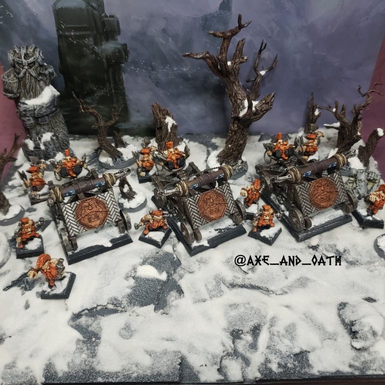 Scenic Warhammer The Old World photograph of Dwarf Slayer Doom Seeker Divers positioned on a snowy mountainside. Three converted Grudge Thrower war machines crewed by Doomseekers and Slayer Engineers stand among snow-covered trees, with a vast mountain pass in the distance. Harsh winter weather, swirling snow, and strong winds create a bleak Karak Kadrin alpine battlefield atmosphere inspired by Warhammer Fantasy and the Gotrek and Felix novels.