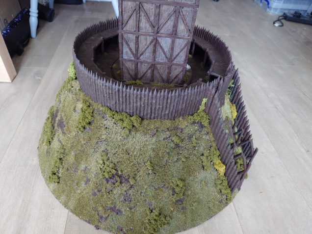 Well I never realised how long it would take to flock this mound. I started off by adding bushes and grass tufts around the base of the pallisades. Then I added random brushes and grass tufts around the mound. This was all done with UHU as it had far better initial adhesive properties than PVA. Once that was done I mixed up some random flocking options and then used some dark green static grass and went around the mound adding PVA and sprinkling on the flocks. This whole process took around 8 hours to do. 