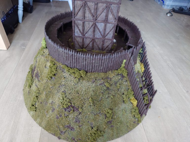 Well I never realised how long it would take to flock this mound. I started off by adding bushes and grass tufts around the base of the pallisades. Then I added random brushes and grass tufts around the mound. This was all done with UHU as it had far better initial adhesive properties than PVA. Once that was done I mixed up some random flocking options and then used some dark green static grass and went around the mound adding PVA and sprinkling on the flocks. This whole process took around 8 hours to do. 