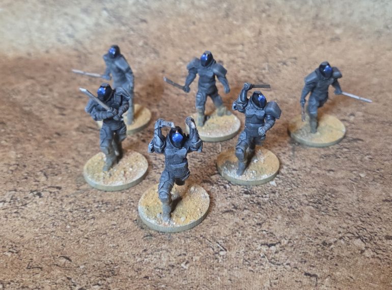 The Bad Guys. Drybrushed black through grey, given a wash of WP Grimdark Shadow wash. Visors painted black, highlights, WP The Darkness, Two Thin Coats Marine Blue, then adding white upto a final very pale blue dot.