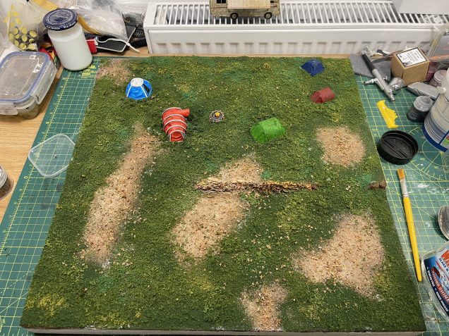 cover the board with PVA then sieve, sprinkle and scatter all sorts of flocks, mud and tile grout mix and also silver birch seeds